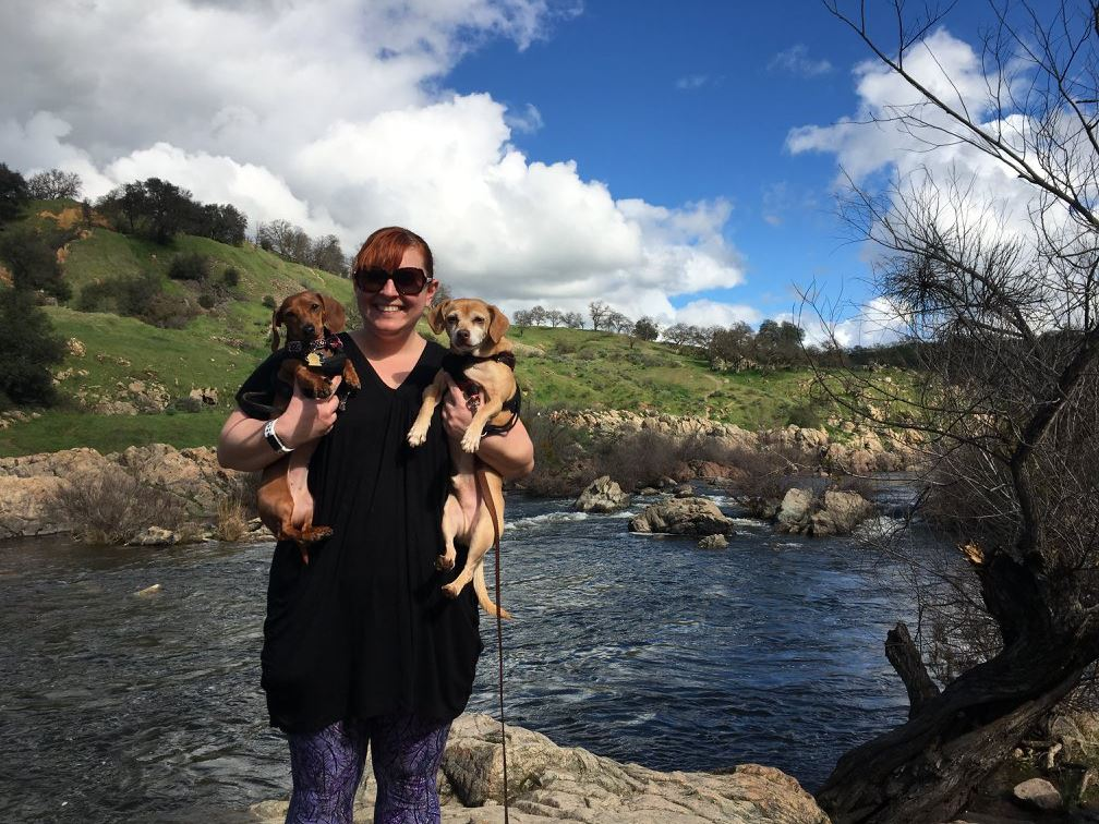 Katie holding 2 dogs by a river